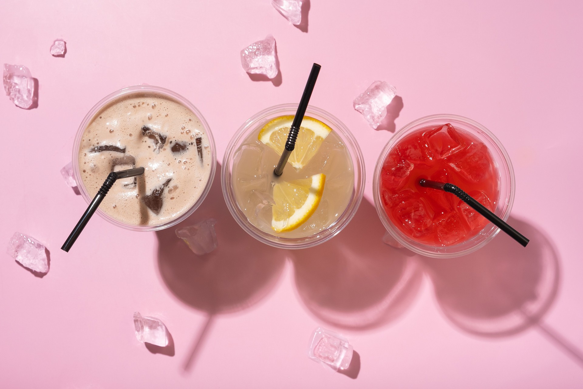 Three takeaway glasses of summer drinks with ice top view. Lemonade on colored background